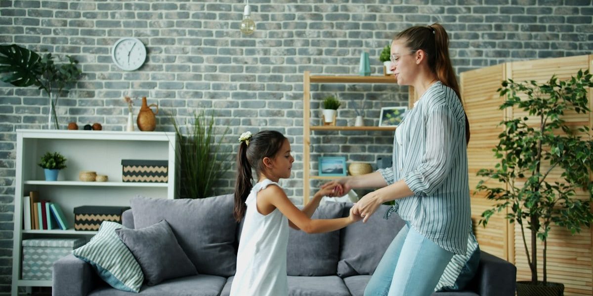 Mom active young woman is dancing with cute little daughter at home jumping having fun bonding enjoying leisure time together. Indoors activity and relaxation concept.