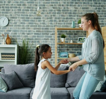 Mom active young woman is dancing with cute little daughter at home jumping having fun bonding enjoying leisure time together. Indoors activity and relaxation concept.