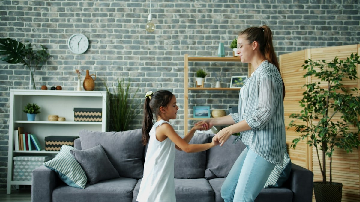 Mom active young woman is dancing with cute little daughter at home jumping having fun bonding enjoying leisure time together. Indoors activity and relaxation concept.
